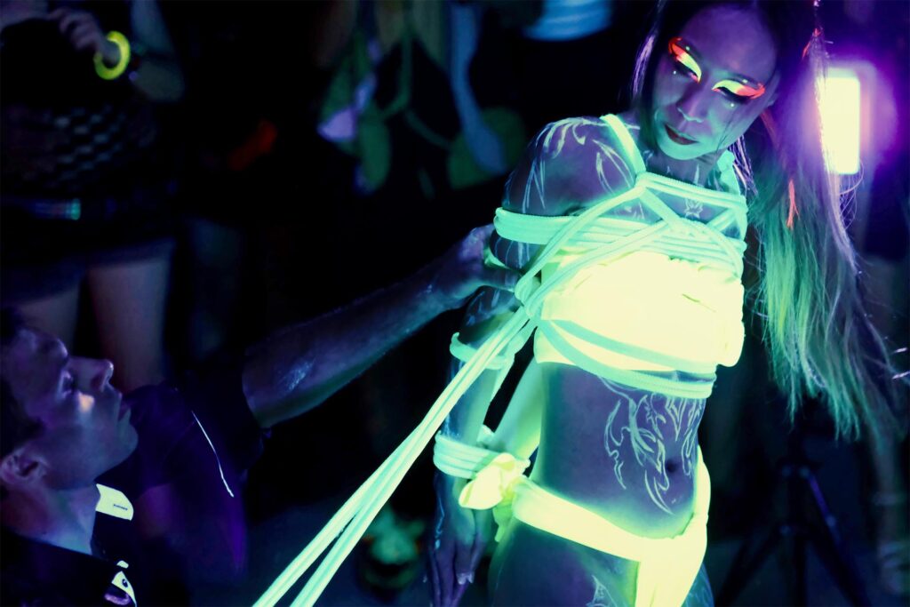UV shibari performance by Louis Kordexe in Tokyo, featuring a model tied with glowing ropes and body paint under blacklight during a live show.