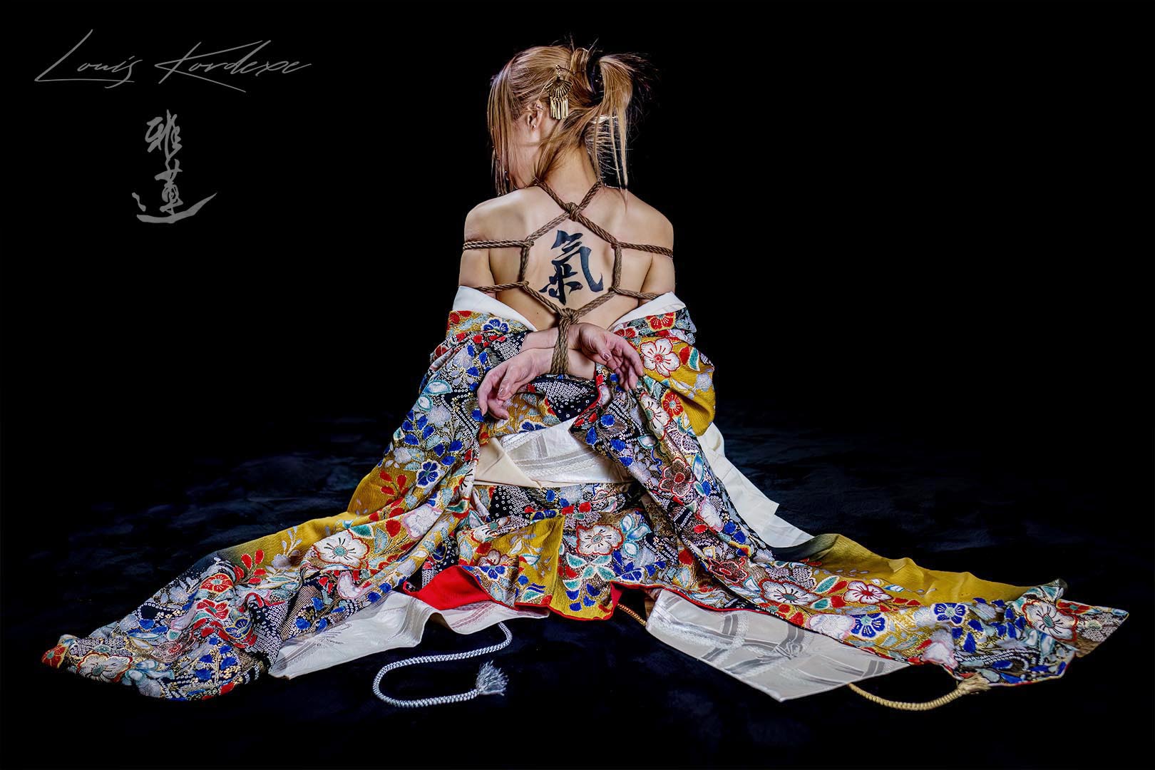 An artistic shibari geibaku back tie by Louis Kordexe, featuring Japanese calligraphy and a traditional decorative kimono in a Tokyo studio.