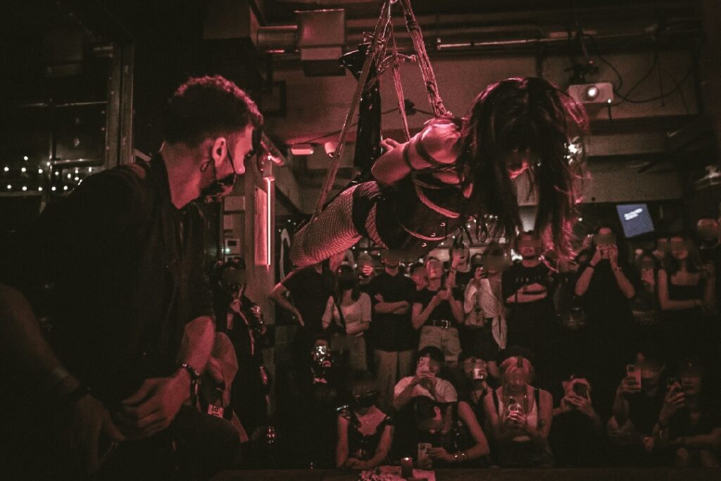 Shibari performance by Louis Kordexe in a Tokyo club, with a crowd watching the live rope show.